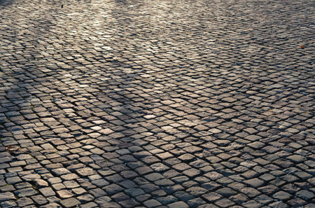 An empty old uneven cobblestone street pavement under sunlightの写真素材
