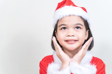 A cheerful Asian female kid wearing Santa Claus clothes on the white backgroundの写真素材