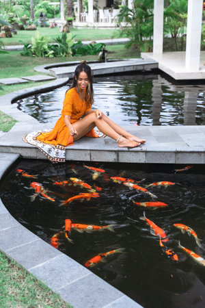An Asian woman feeding fishes in the poolの写真素材
