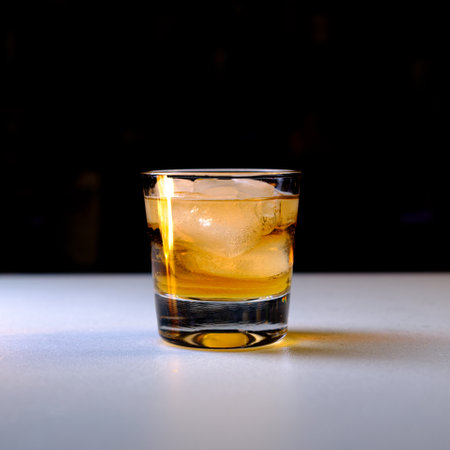 A closeup of a glass of cold iced whiskey on the table against a black background