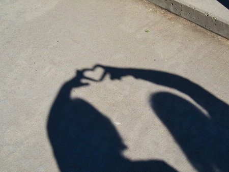 The shadows of two people joining hands to create a heart symbol on the groundの写真素材