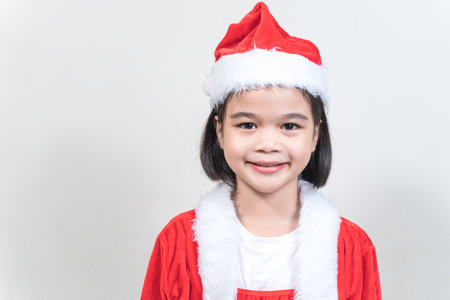 A cheerful Asian female kid wearing Santa Claus clothes on the white backgroundの写真素材