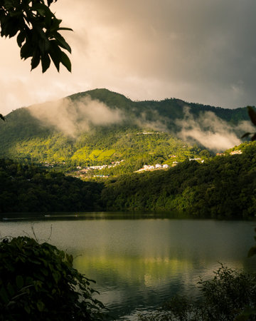 A vertical shot of lakeshore with green mountains and fogの写真素材