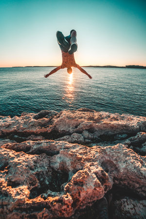 A male doing a backflip off a cliff against the sinking sunの写真素材