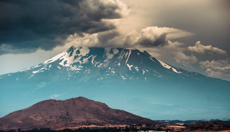 A mesmerizing view of a huge mountain covered in snow with a small hill in the foreの写真素材