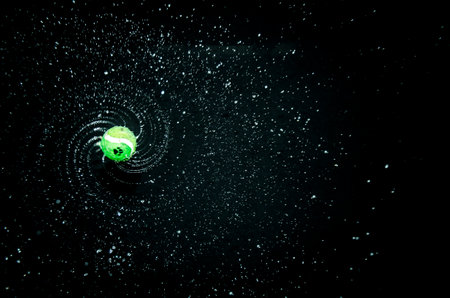 A studio shot of a tennis ball thrown into the air with waterdrops spreading on the black backgroundの写真素材