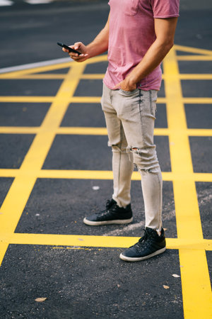 A vertical shot of a young Caucasian male wearing a pink t-shirt texting on the phone on a streetの写真素材