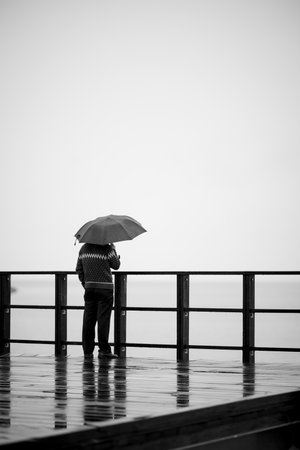 A vertical back view of a person with an umbrella enjoying a rainy day on the pierの写真素材