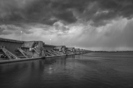 A grayscale shot of a calm sea with a pier under a cloudy skyの写真素材
