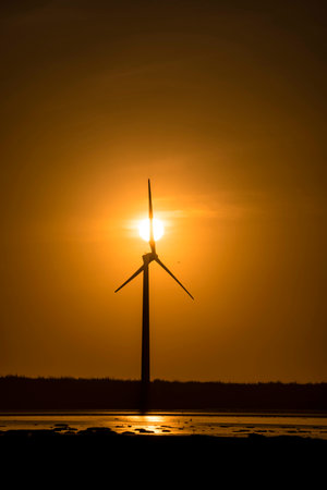 A vertical shot of a wind turbine on a shore under a shining sunの写真素材