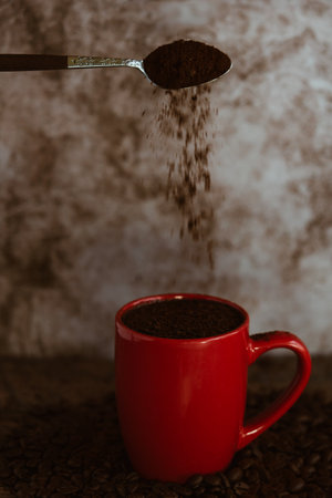 A vertical shot of a spoon with coffee pouring in the cupの写真素材