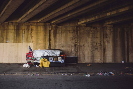 An old sofa under with some old stuff, Jesus picture under a bridge in a dirty street with rusty...