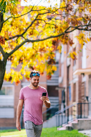 A vertical shot of a young Caucasian male wearing a pink t-shirt texting on the phone on a street