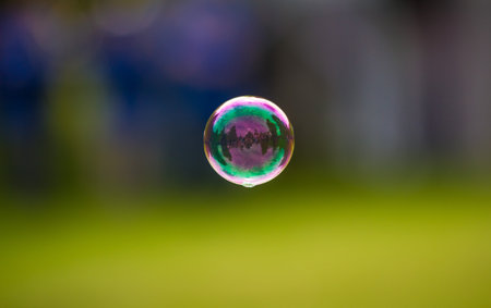 A closeup of a floating soap bubble against a blurry nature backgroundの写真素材