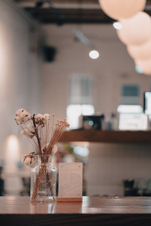 A closeup shot of a cafe wooden table with a jar of decorative flowers against a blurred backgroundの写真素材