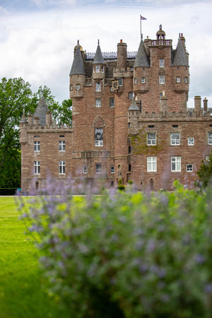 A vertical shot of Glamis Castle with green fields under a blue cloudy sky in Scotlandの写真素材