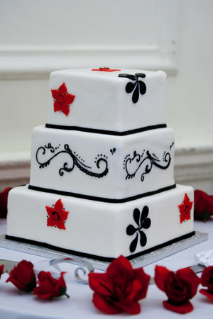 A vertical shot of a red, black and white wedding cake on a tableの写真素材