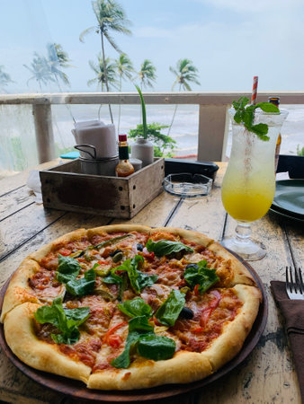 A vertical shot of a pizza with arugula and fresh lemonade in the restaurant near the seaの写真素材