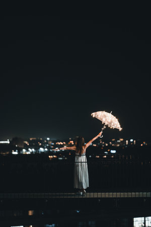 A female with a magical umbrella standing on the bridge at nightの写真素材
