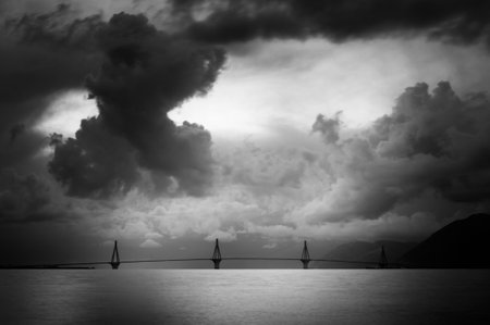 A grayscale shot of Rio Antirrio bridge with storm clouds in the backgroundの写真素材