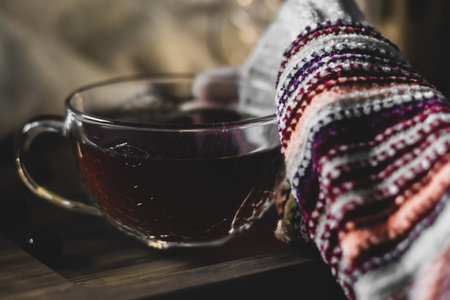 A closeup shot of a hand wearing a warm sweater and holding a glass of tea