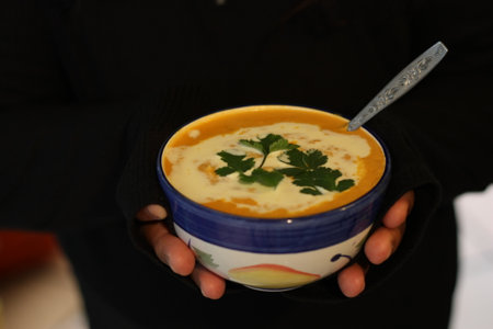 A closeup of a person holding a bowl of pumpkin soupの写真素材