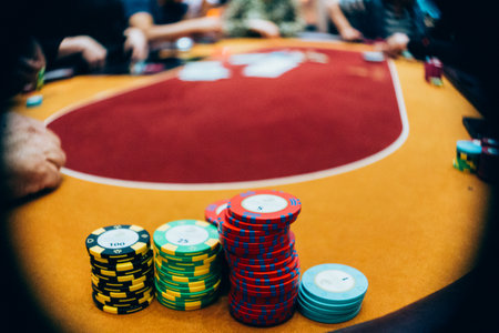 A close-up shot of poker chips on the table with people playing Texas Hold 'Em, on the background