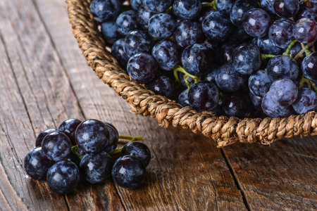 A wicker plate full of fresh ripe black grapes on a wooden tableの写真素材