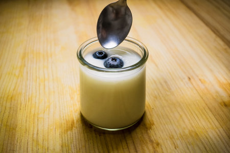 A small cup of homemade yogurt with blueberries on a wooden tableの写真素材