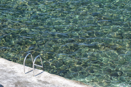 High view of a metal ladder leading into a clear seawater pool.の写真素材