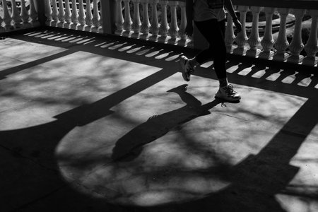 A grayscale shot of a shadow of a young female walking in the street near the arched columnsの写真素材