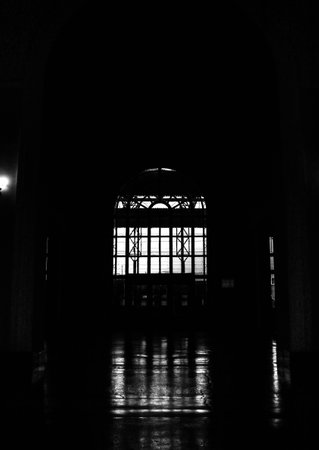 A vertical shot of a dark corridor with an arched window in the end with a metal gridの写真素材