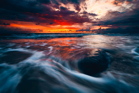 A mesmerizing view of the Sunset at the coast of the Baltic Sea, Lithuania on rocks in the waterの写真素材