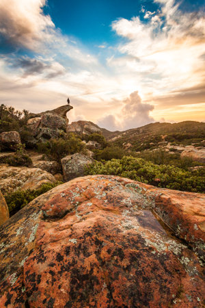 A vertical shot of scenic mountainous nature and a silhouette of a person on an edge of a cliff on a sunsetの写真素材