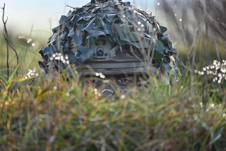A person wearing a camouflage hat hiding behind green grassの写真素材