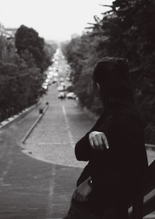 A grayscale shot of a young female looking aside towards the traffic road on a gloomy dayの写真素材