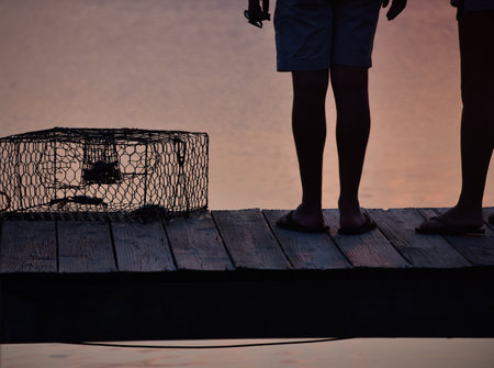 Silhouettes of two people standing on the wooden ground preparing for crabbingの写真素材