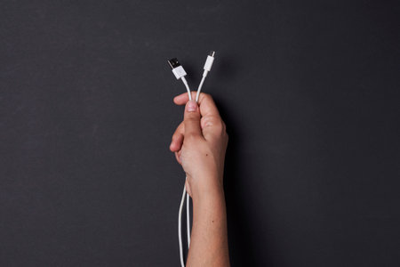A top view of a hand holding white charging wires on a black backgroundの写真素材