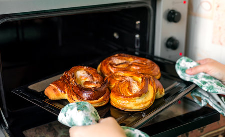 A woman taking out a tray with freshly baked pretzels from an ovenの写真素材