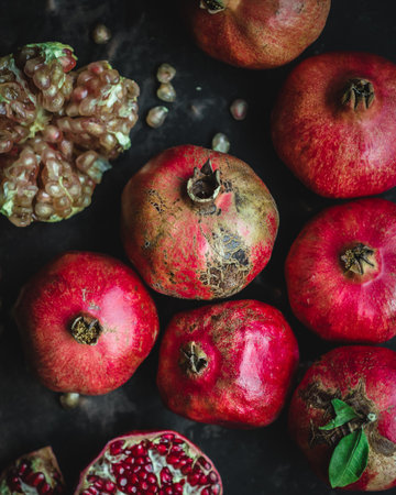 A vertical closeup shot of whole and peeled pomegranates on a black surfaceの写真素材