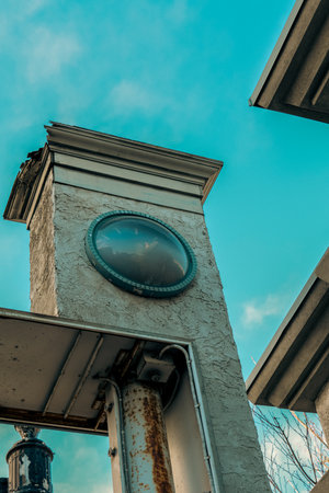 A vertical shot of an old, damaged stucco pillar with a faded clock on its facadeの写真素材