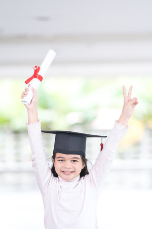 A vertical shot of a happy Southeast Asian schoolgirl with a certificate celebrating graduation in Thailandの写真素材