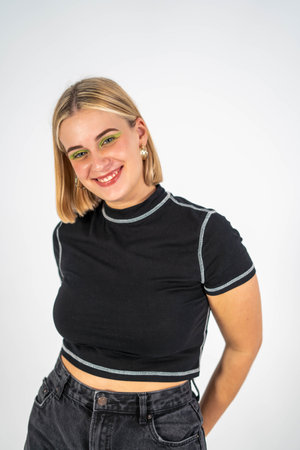 A portrait of young smiling Spanish woman with green shiny eyeshadow posing against a white...