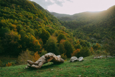 A piece of an old broken statue in a mountainous landscape with trees and greeneryの写真素材