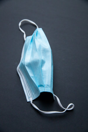 A vertical shto of a medical facemask on a dark surface - COVID