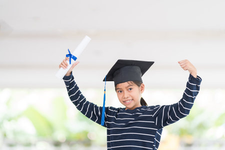 A shallow focus shot of a happy Thai kid with a graduation hat and diplomaの写真素材