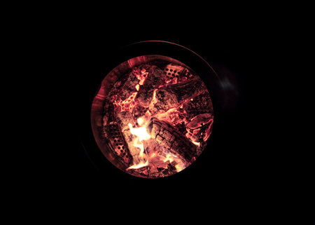 A closeup top view of wood fire flames burning in a pot on a dark background
