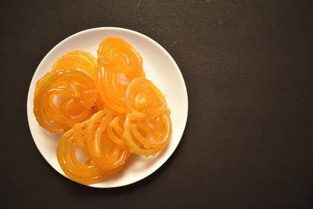 Selective focus picture of Indian Traditional Sweet called Jelebi kept in white plate in flat lay,...