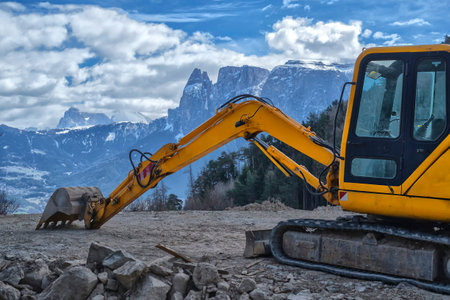 An industrial excavator working on a site with a view of the Dolomites mountainsの写真素材