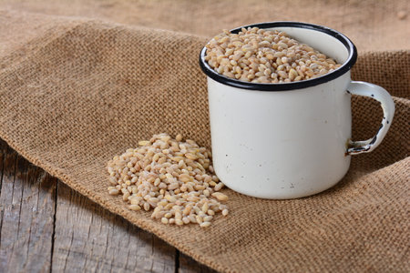 The white enamel mug with pearl barley grains on the wooden tableの写真素材